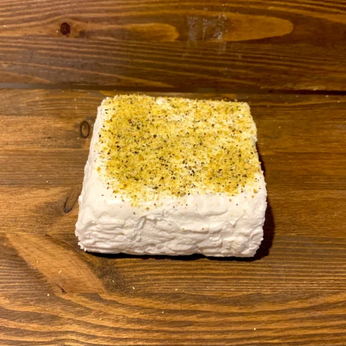 Elegancka kompozycja rustykalnego sera koziego Fromage Yagi z pieprzem cytrynowym na tle ciemnego drewna – naturalny, rzemieślniczy produkt z polskiego gospodarstwa.